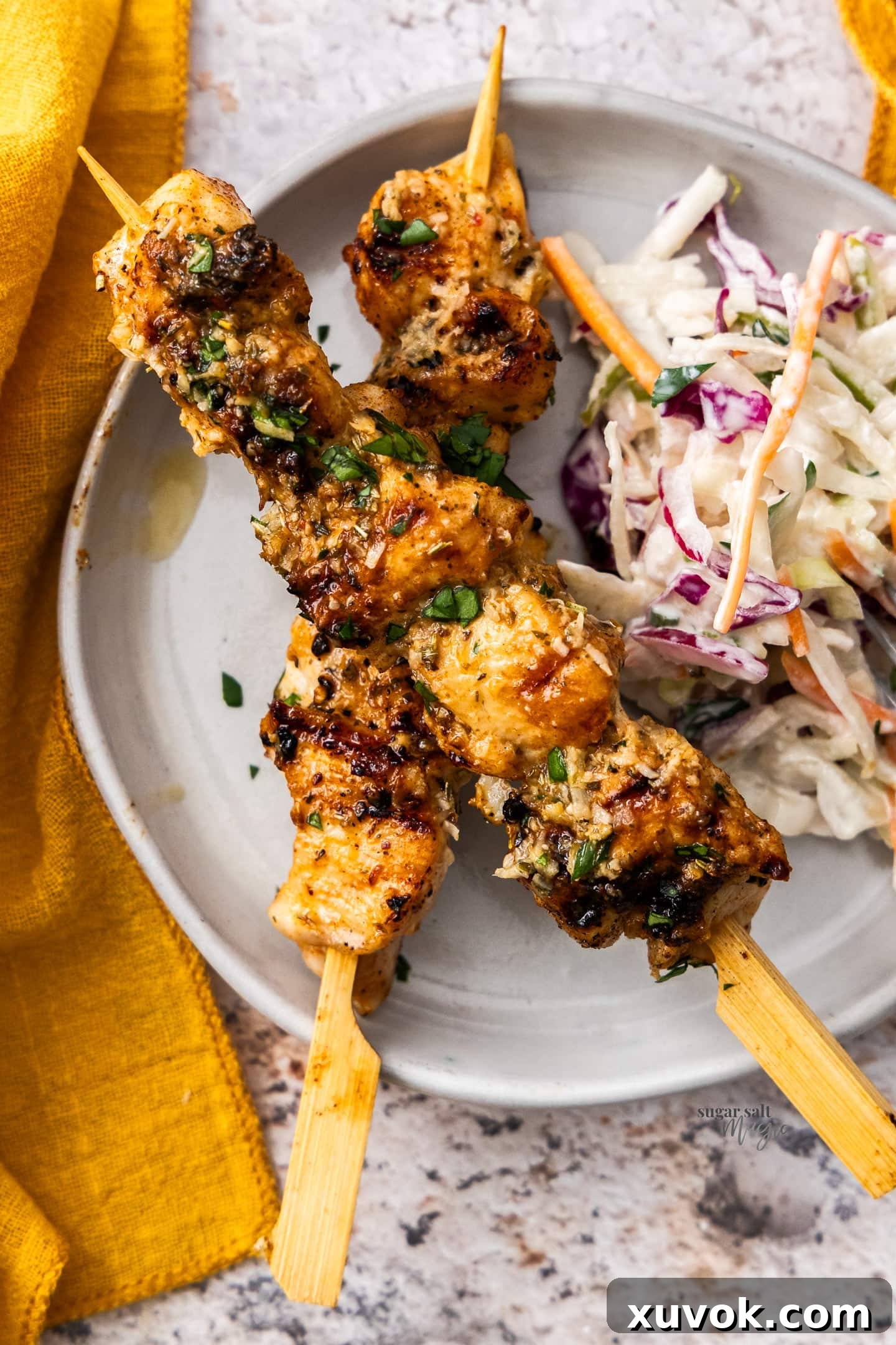 Top down view of two garlic parmesan chicken skewers resting on a plate next to a fresh coleslaw.