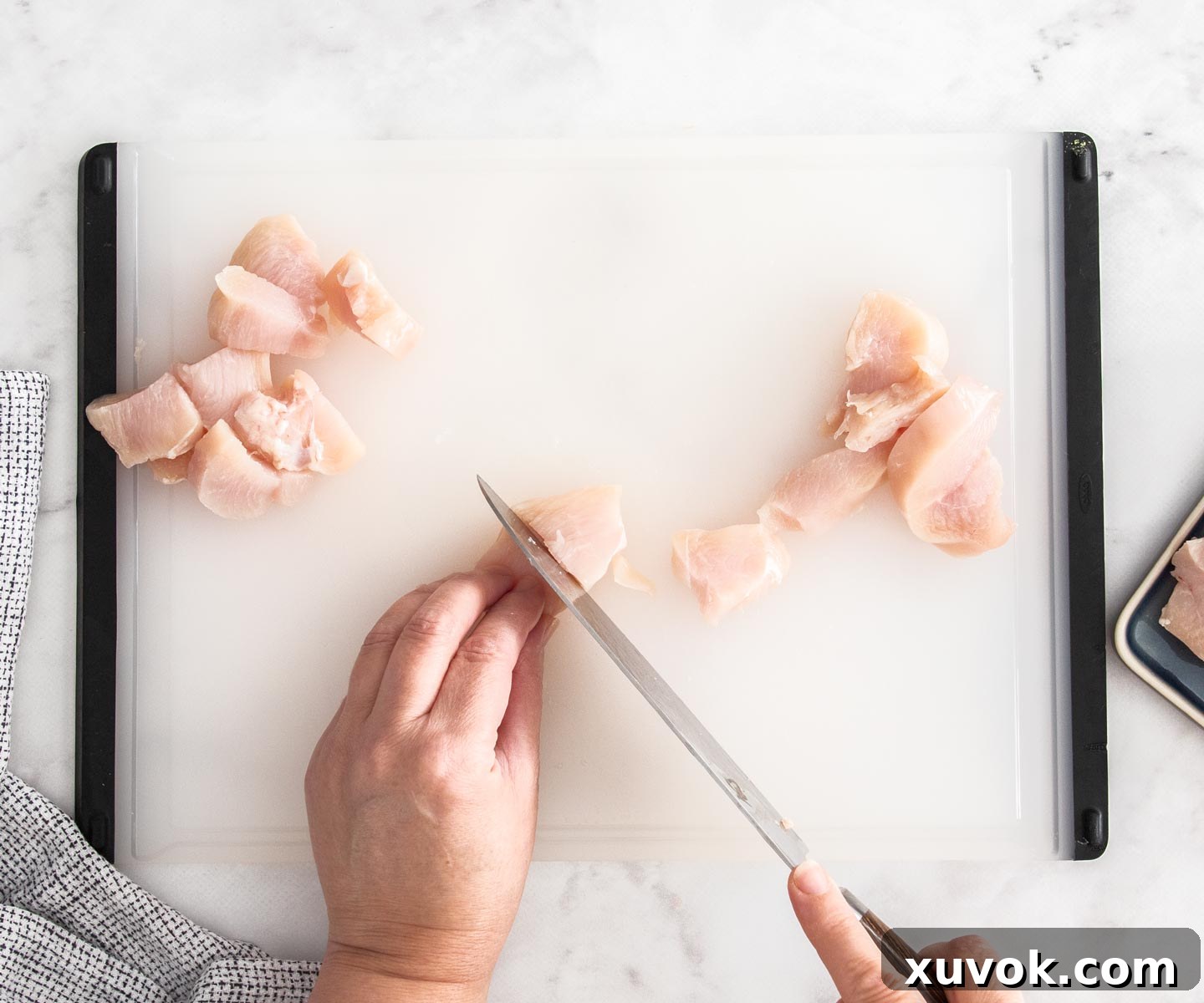 Chicken breast being diced into large, even chunks for skewering.