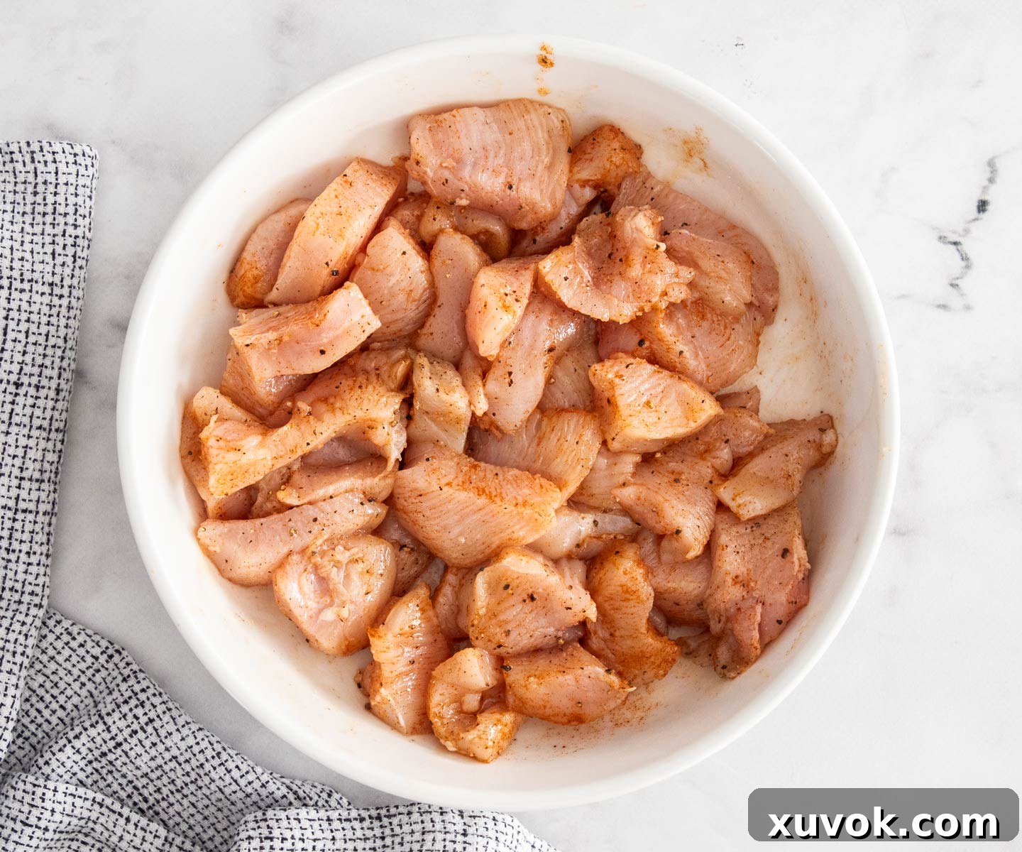 Chunks of seasoned chicken breast glistening in a bowl, ready for skewering.