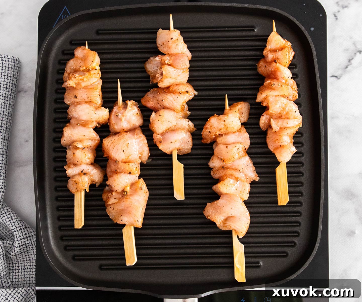 Chicken skewers sizzling and developing a golden crust on a hot grill pan.