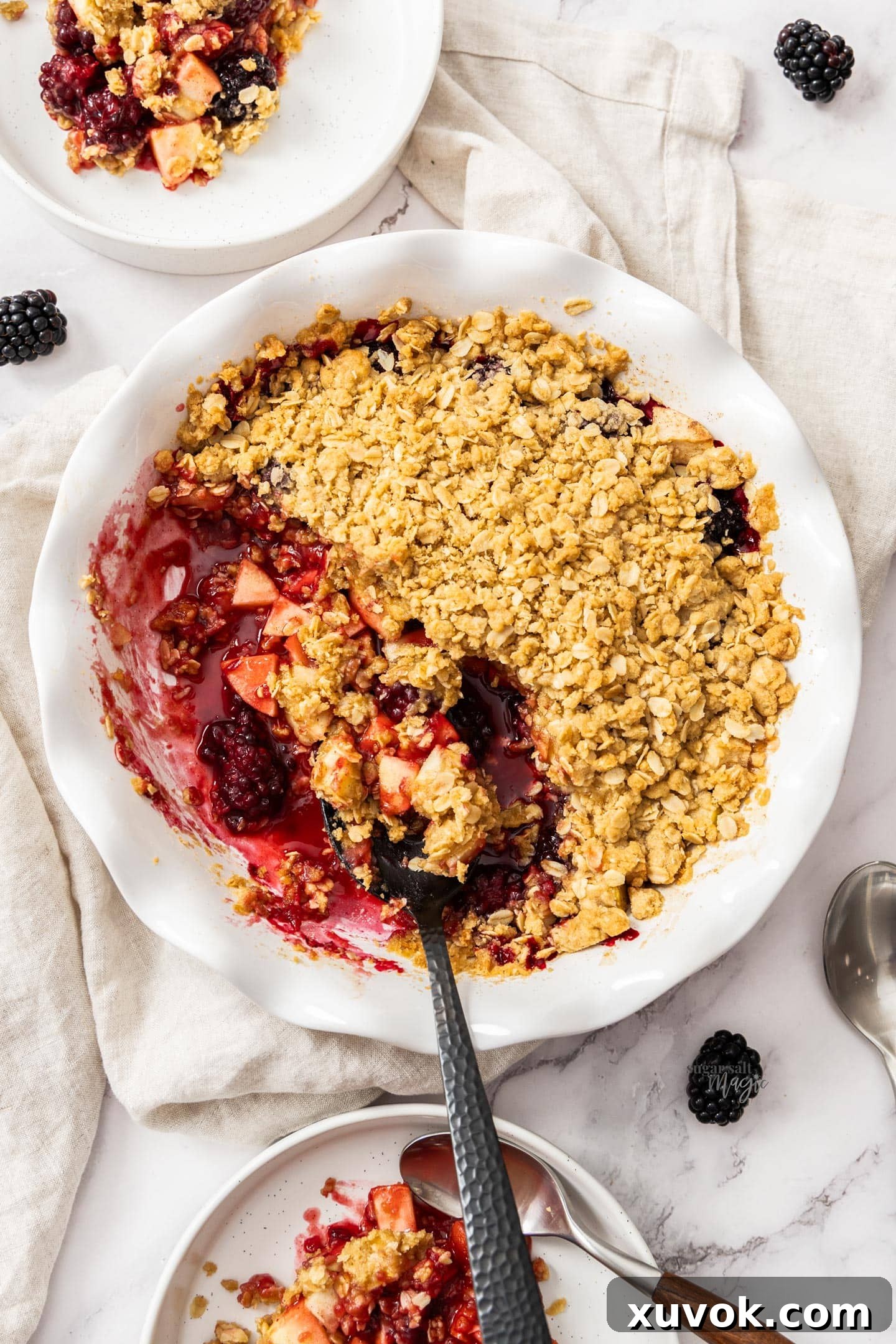 A beautifully baked apple and blackberry crumble, seen from a top-down perspective, showcasing the golden-brown topping and fruit filling.
