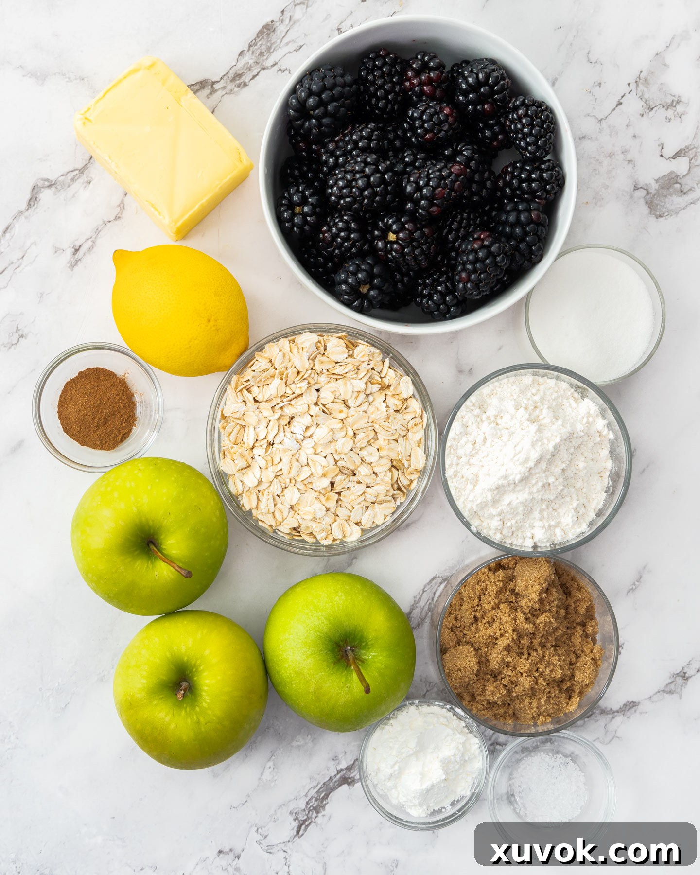 A flat lay photograph of all the fresh ingredients needed for a delicious blackberry apple crumble, arranged on a beautiful marble surface.