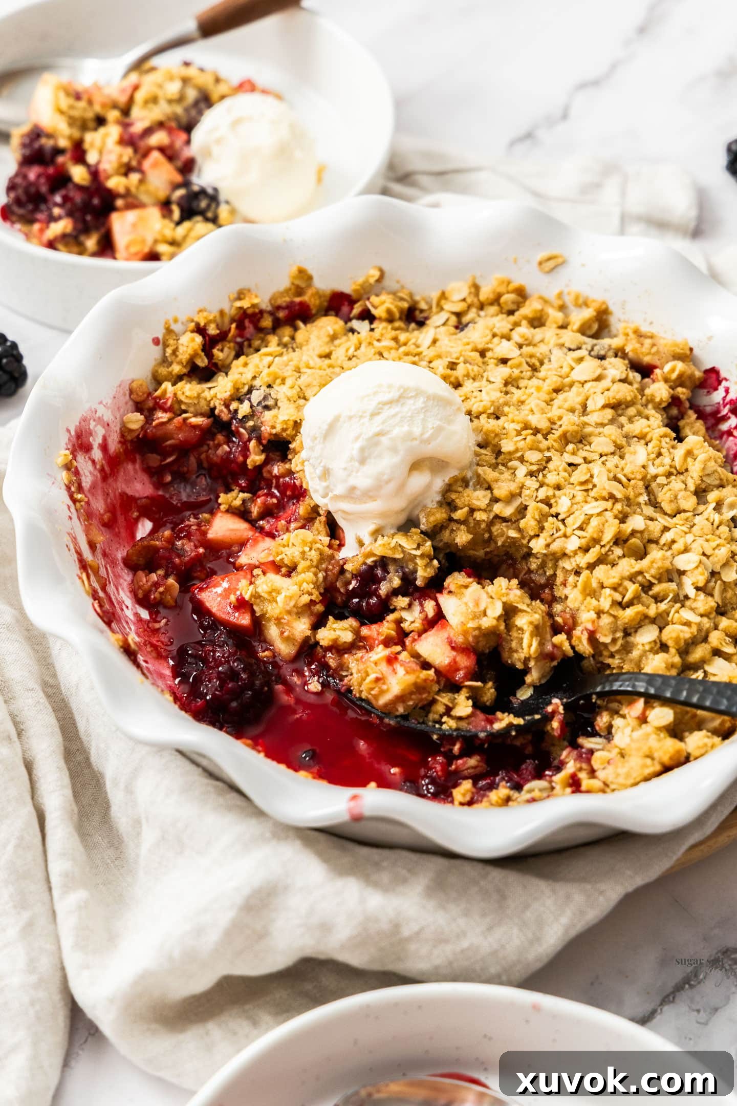 A close-up shot of a steaming hot apple blackberry crumble served in a rustic bowl, topped with a generous scoop of vanilla ice cream, ready to be enjoyed.