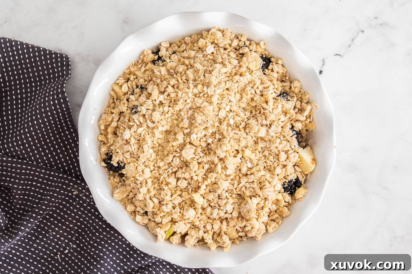 The unbaked apple blackberry crumble in a pie dish, with the streusel topping perfectly distributed over the fruit.