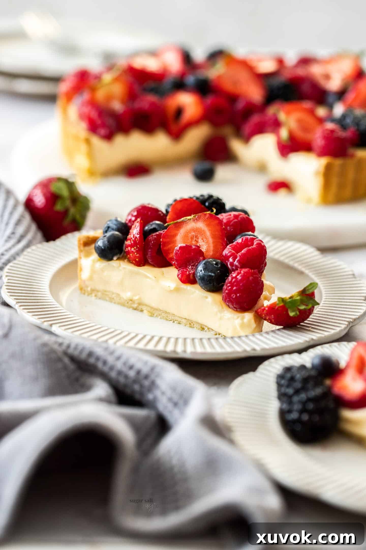 A beautifully presented slice of fruit custard tart on a small dessert plate, garnished with fresh berries, showcasing the crisp pastry and creamy filling.