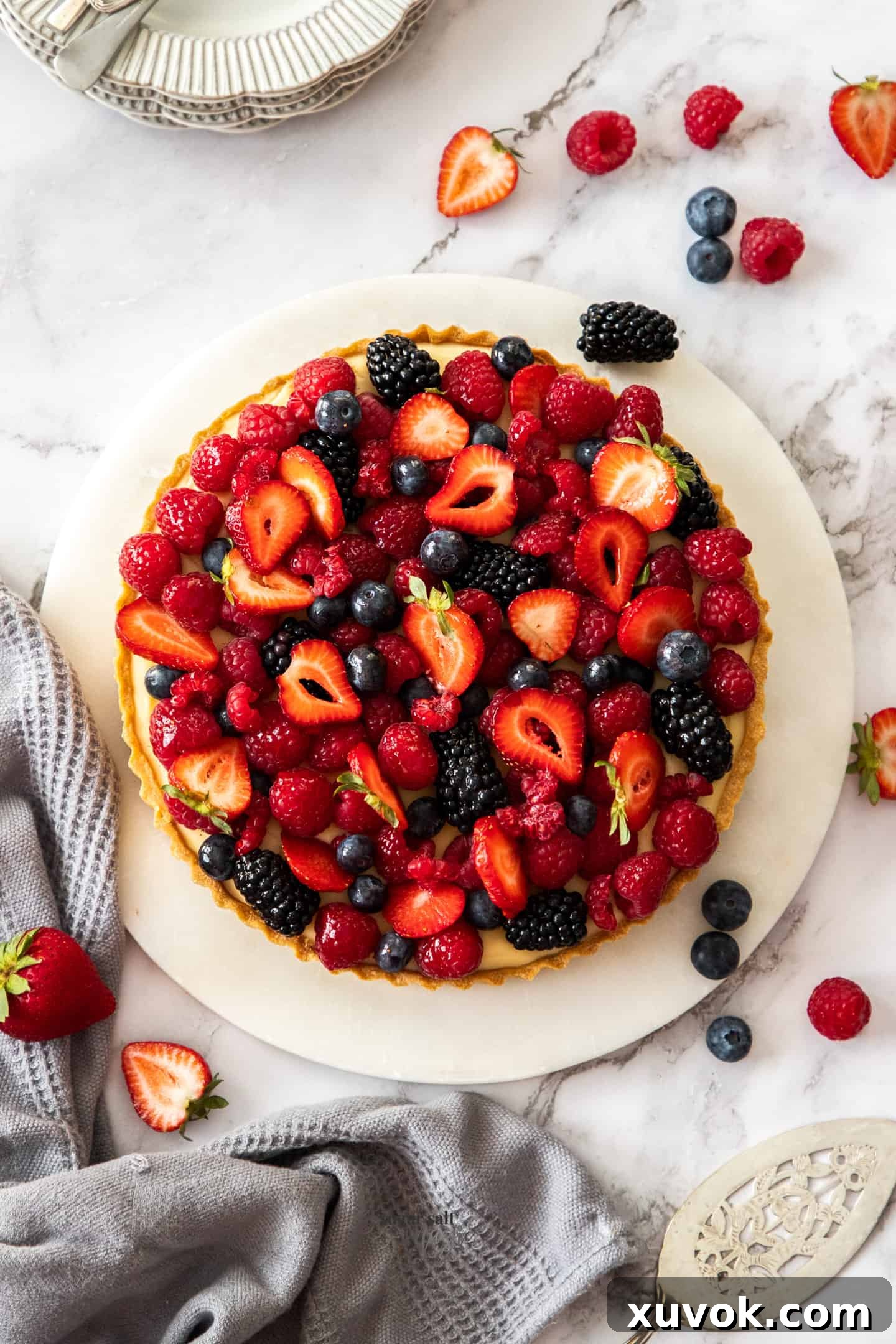 A vibrant top-down view of a completed fruit custard tart, generously topped with an assortment of fresh berries, ready to be served.