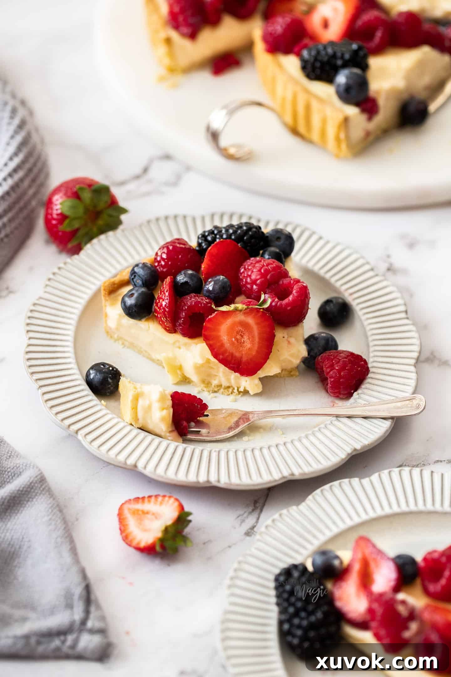 A perfectly cut slice of fruit custard tart on a white plate, with a forkful ready to be enjoyed, highlighting the creamy texture and fresh fruit.