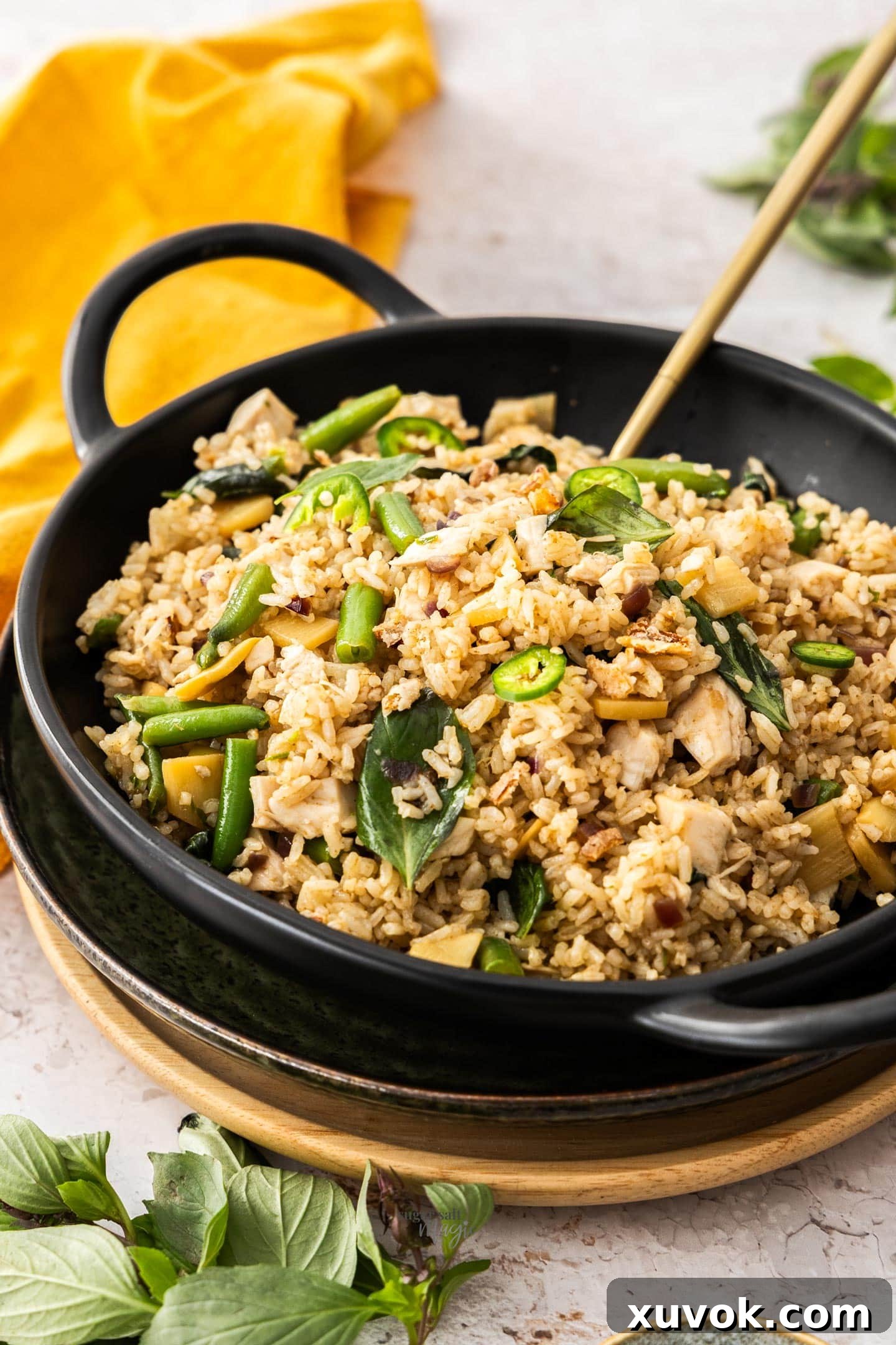 A black bowl filled with aromatic Thai green curry fried rice, generously topped with vibrant green chili slices, ready to be enjoyed.