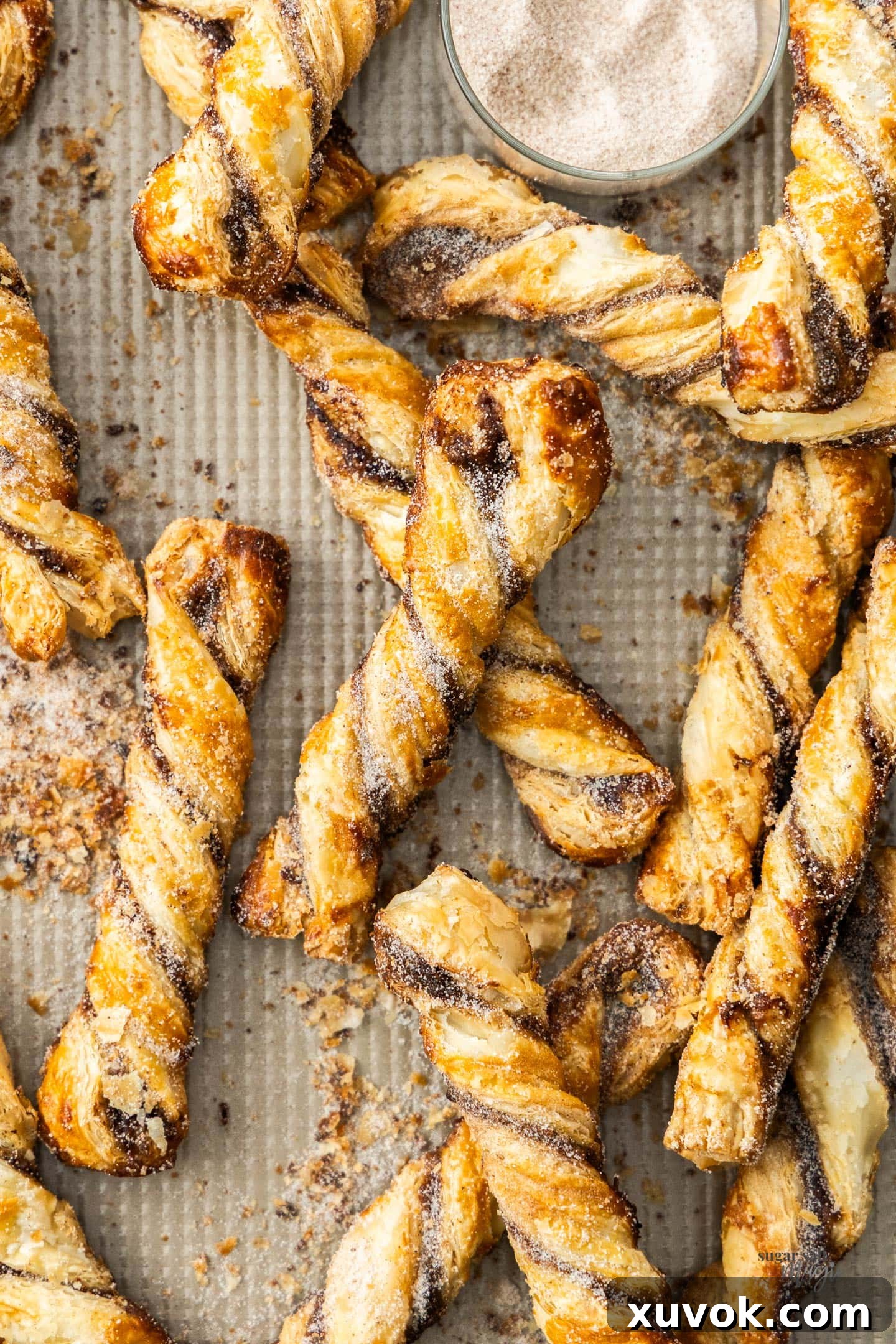 Top-down view of freshly baked cinnamon puff pastry twists arranged on a baking tray, showcasing their golden-brown color and spiral shape.