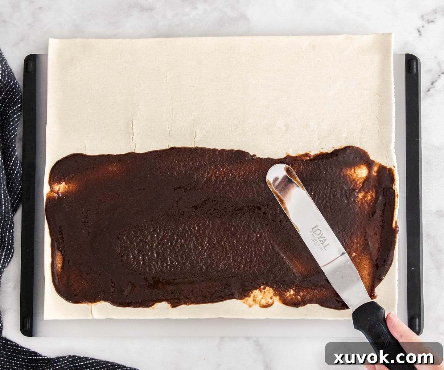 The cinnamon sugar mixture being evenly spread over one half of a rectangular puff pastry sheet.