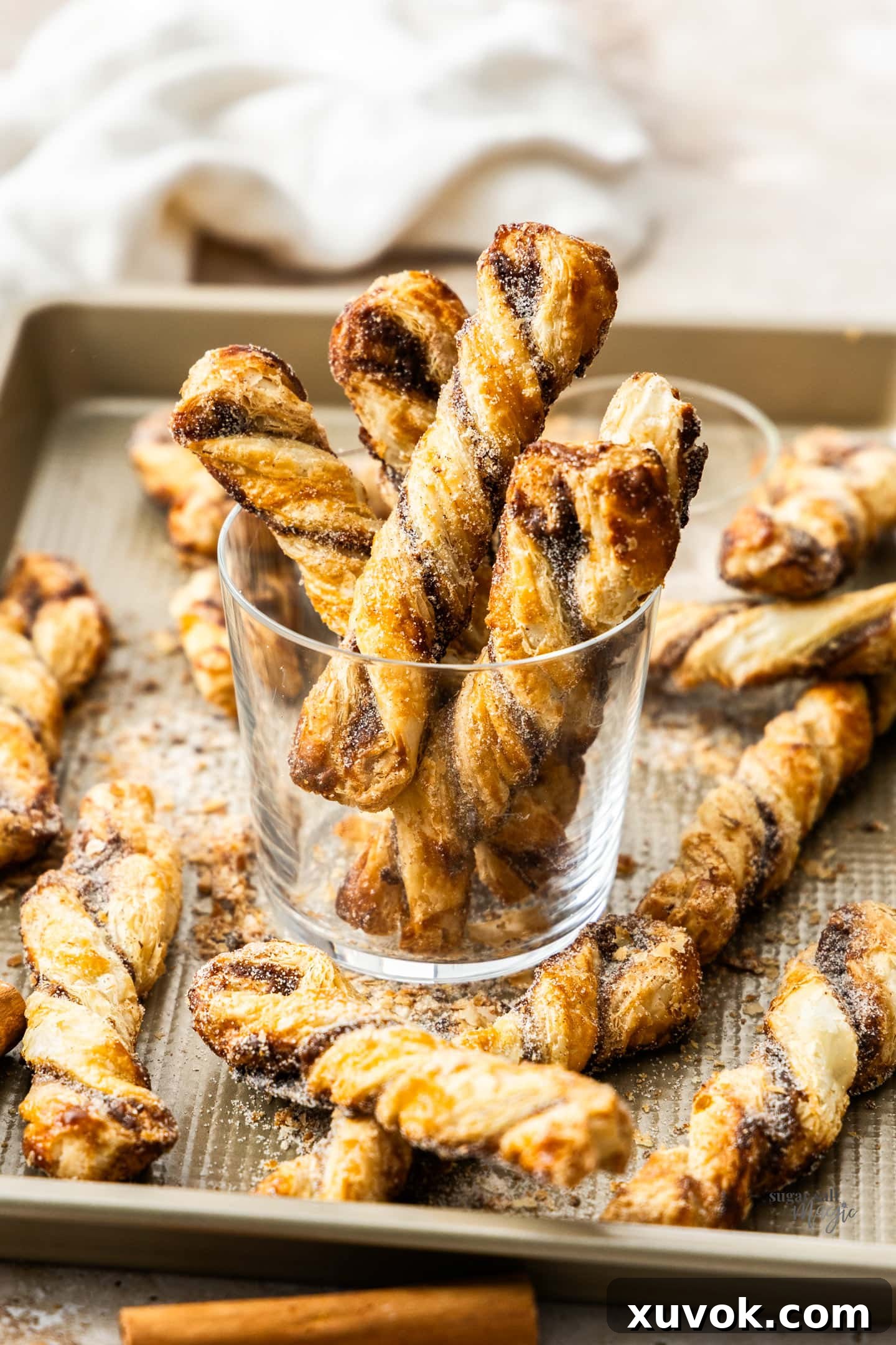 Five golden-brown cinnamon puff pastry twists arranged in a glass, sitting on a baking tray.