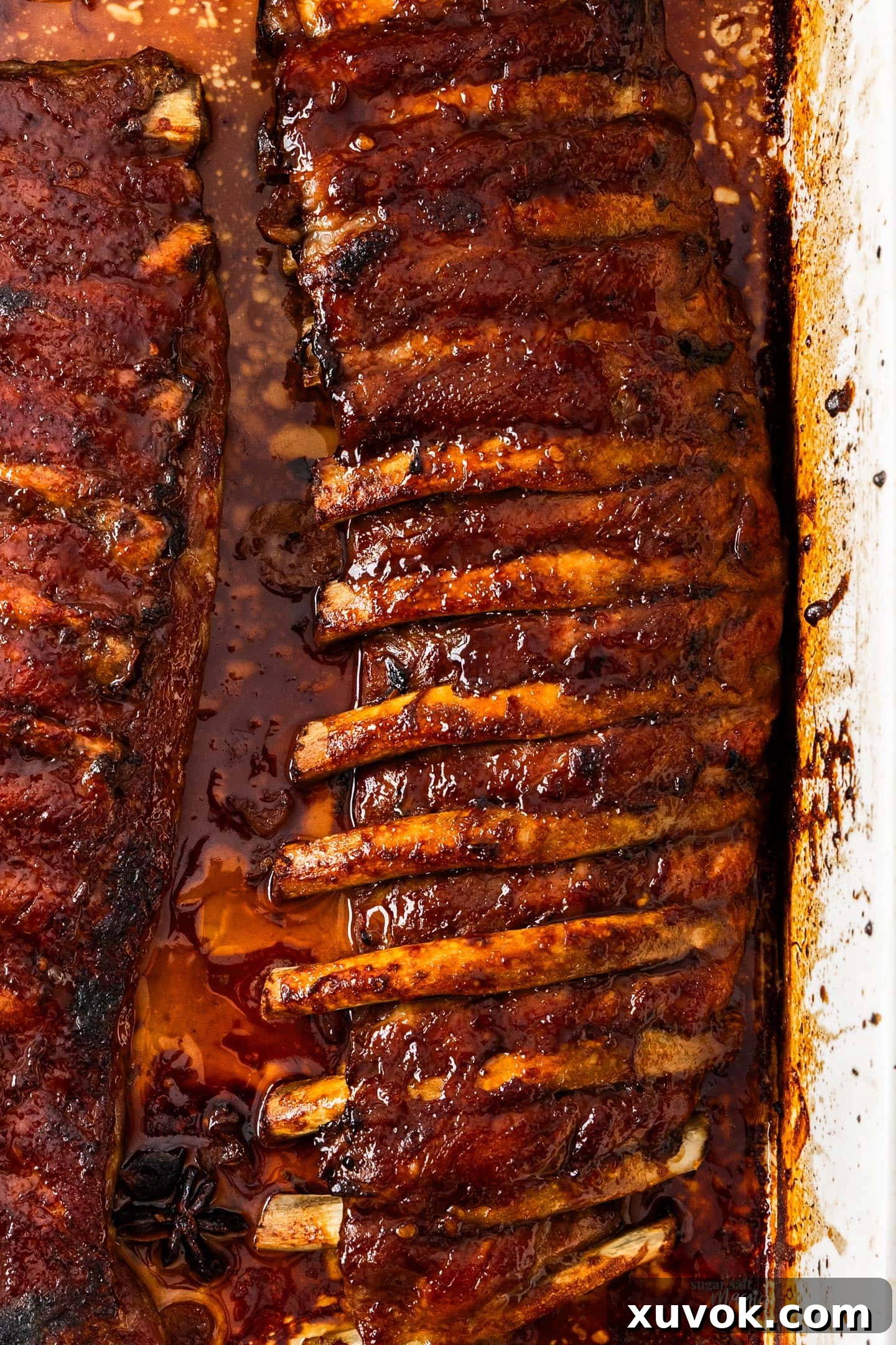 Top down view of sticky asian pork ribs in a baking dish, garnished with sesame seeds and green onions.
