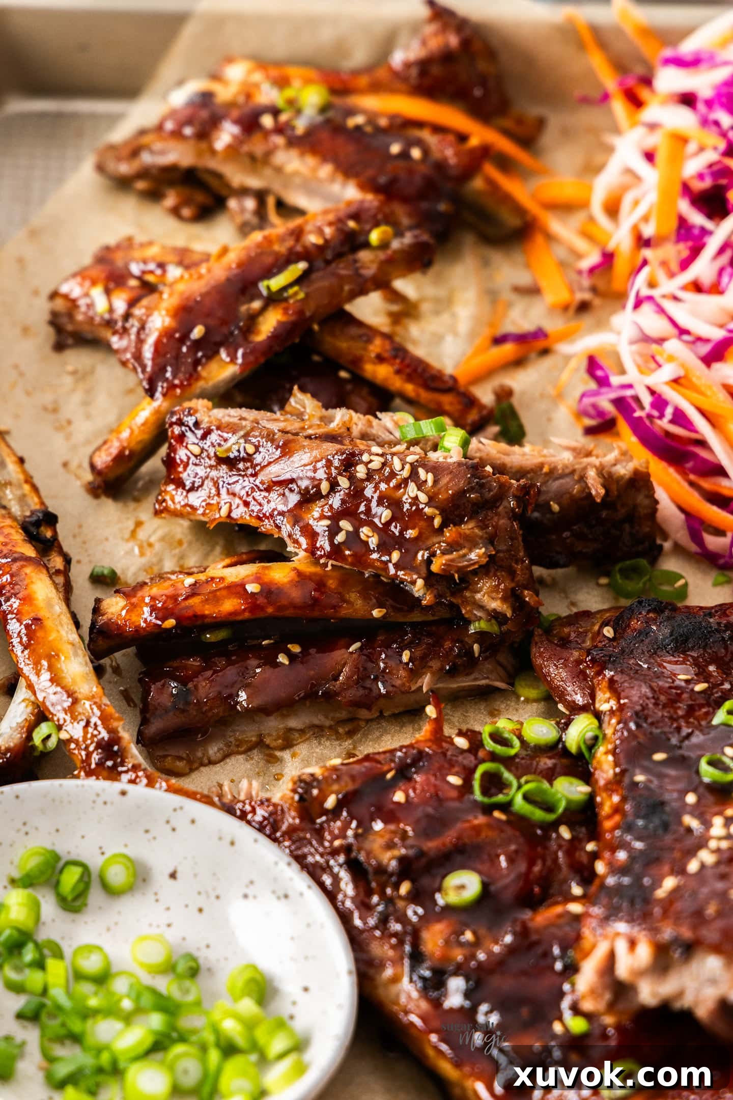 The cooked asian sticky ribs torn apart on a tray, ready to eat, garnished with green onions.