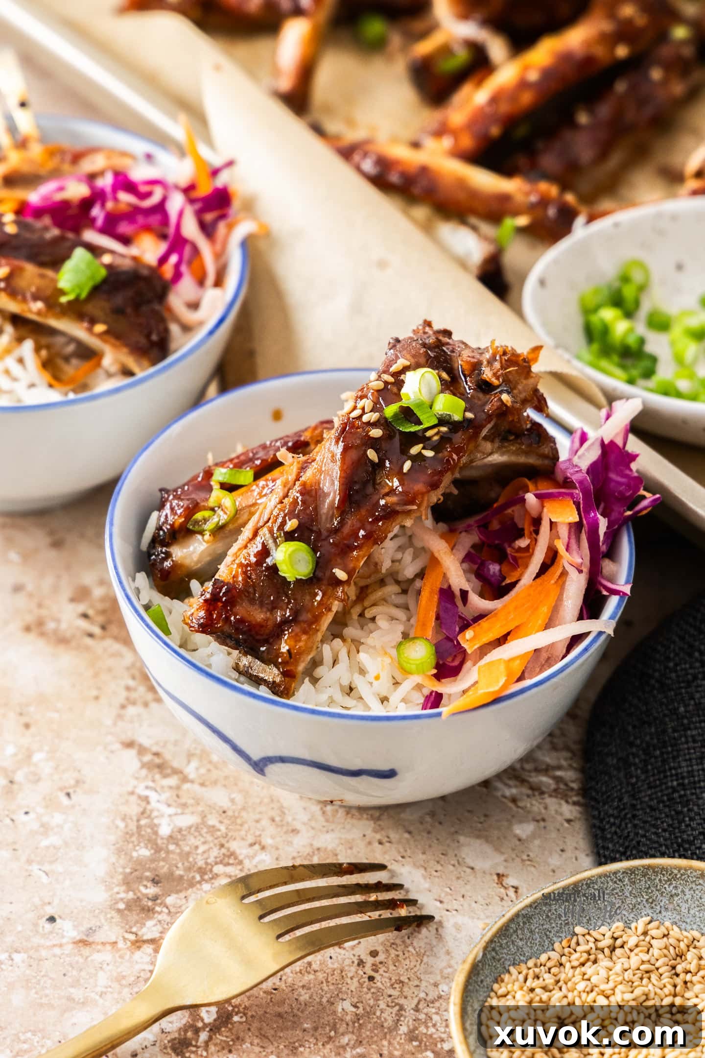 Some sticky asian pork ribs on top of a small bowl of steamed rice, garnished with green onions.