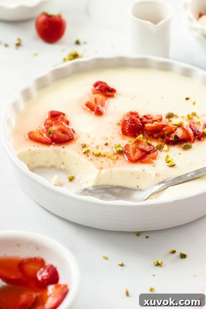 A large white dish filled with strawberry panna cotta, garnished with fresh macerated strawberries. A spoon is resting in the dish.