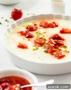 A large white dish filled with panna cotta. Some macerated strawberries sit on top and in front.