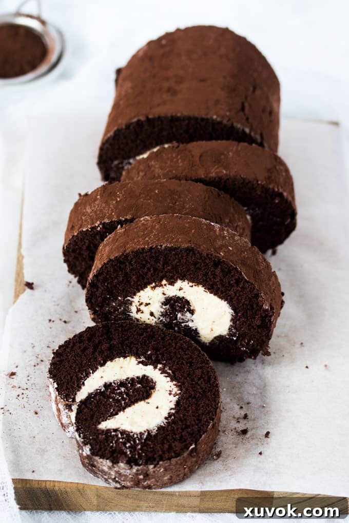 A chocolate roll cake cut into slices on a sheet of baking paper, showcasing its beautiful spiral.