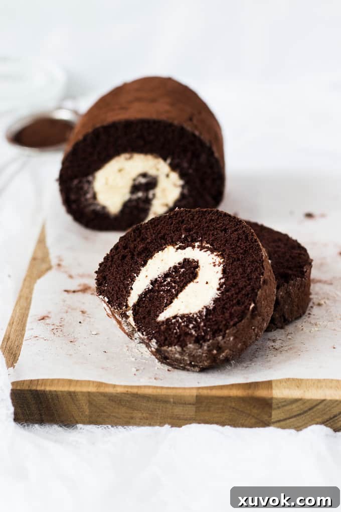 Slices of chocolate roll cake stacked againsted one another on a wooden board, showing the filling.