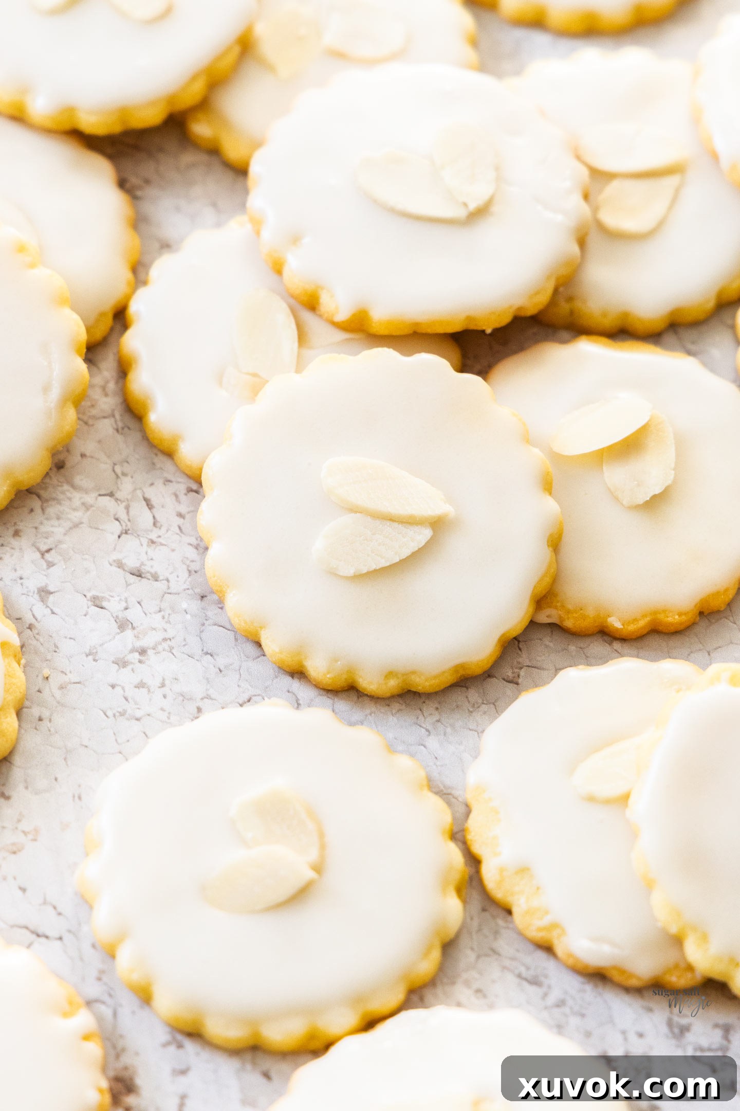 A pile of almond cookies topped with icing and flaked almonds, showcasing their delicate texture and beautiful presentation.