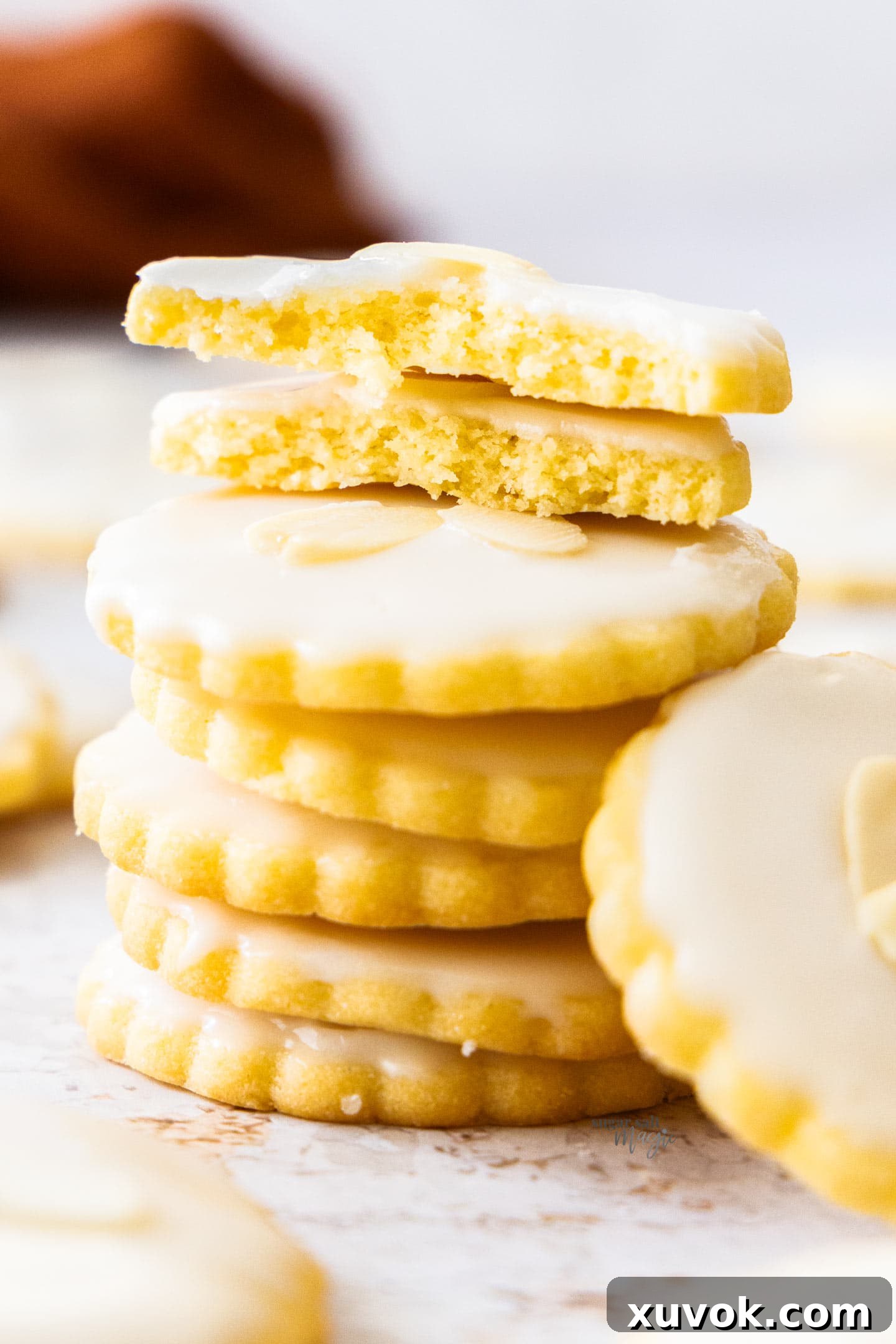 A pile of almond cookies with the top one broken in half to show the soft, tender texture inside, with flaked almonds on top.