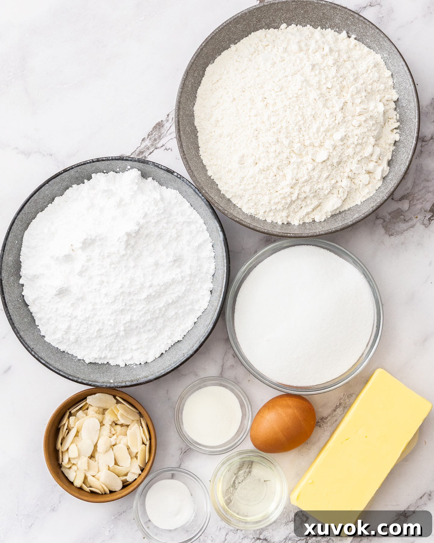 A flat lay of fresh ingredients for almond sugar cookies, including butter, sugar, eggs, flour, and almond extract, ready for baking.