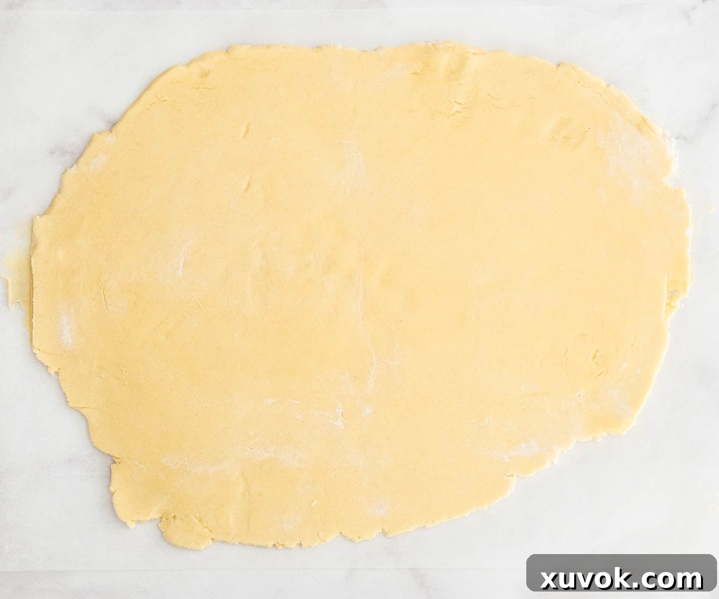 Cookie dough rolled out evenly between two sheets of baking paper on a marble surface, ready for chilling.