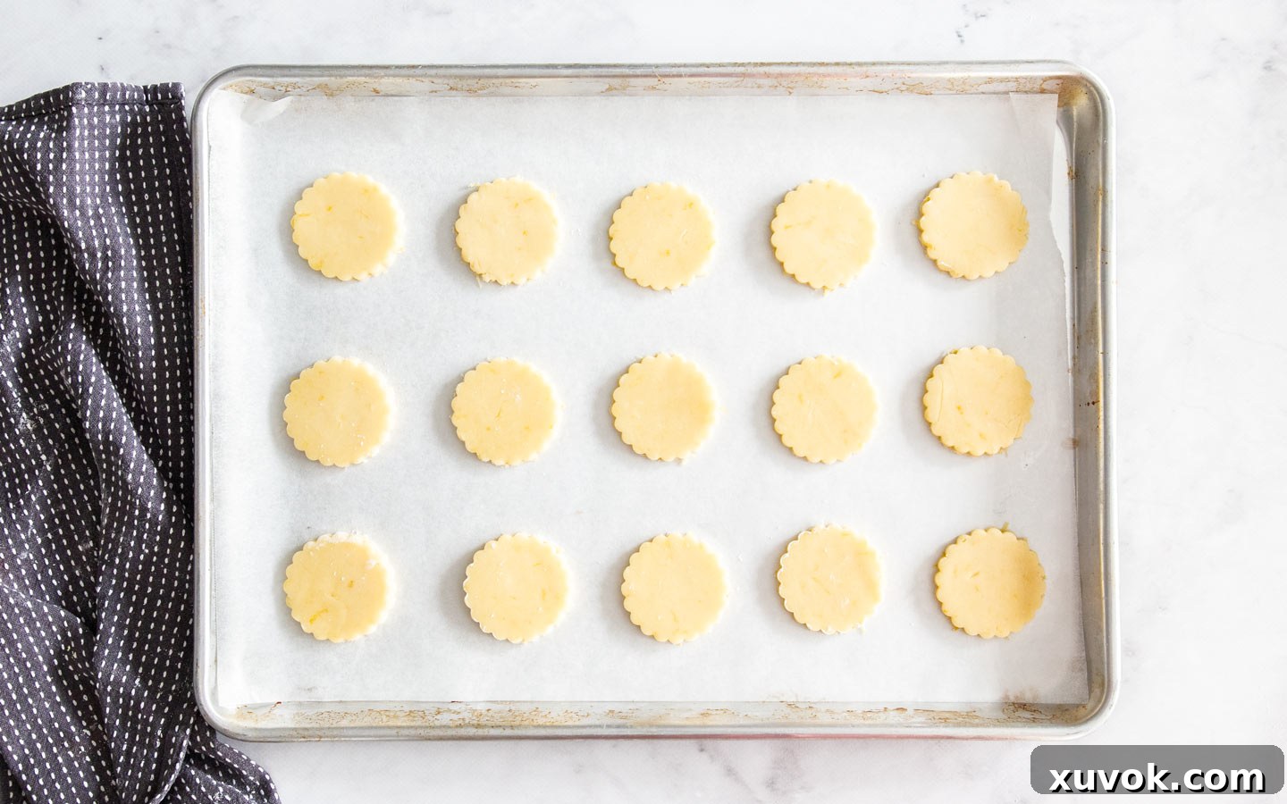 Raw, cut-out almond cookies arranged on a baking sheet lined with parchment paper, ready to go into the oven.