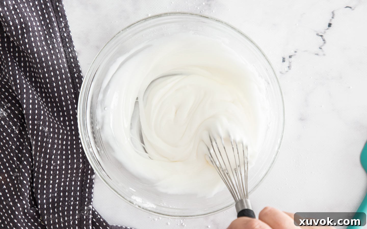 Whisking royal icing in a bowl, demonstrating the smooth texture and readiness for dipping cookies.