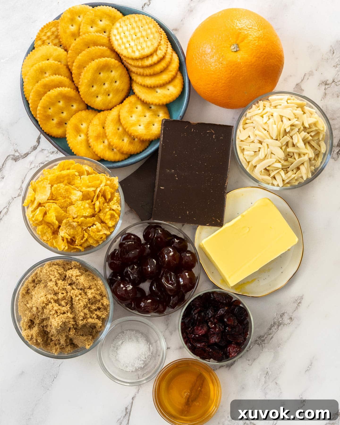 Ingredients for florentine slice laid out on a table, including crackers, almonds, dried fruit, butter, sugar, honey, and chocolate.