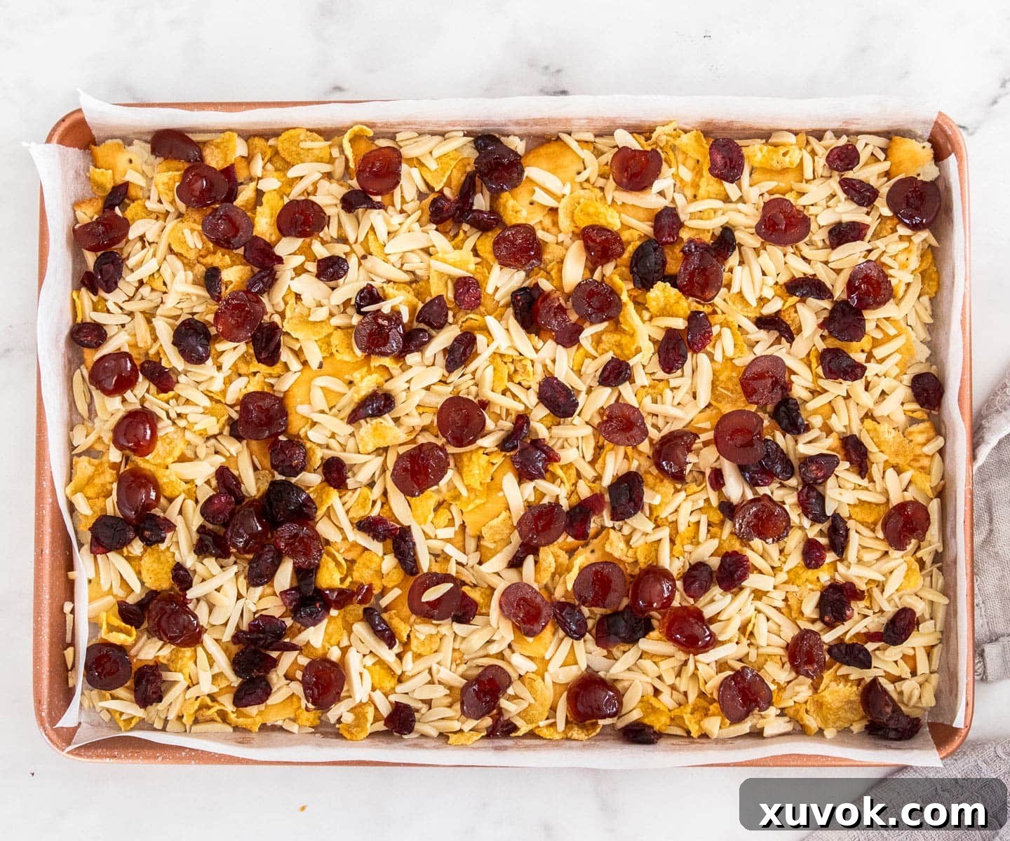The other filling ingredients, including almonds, cornflakes, and dried fruits, scattered over the cracker base in the baking tray.