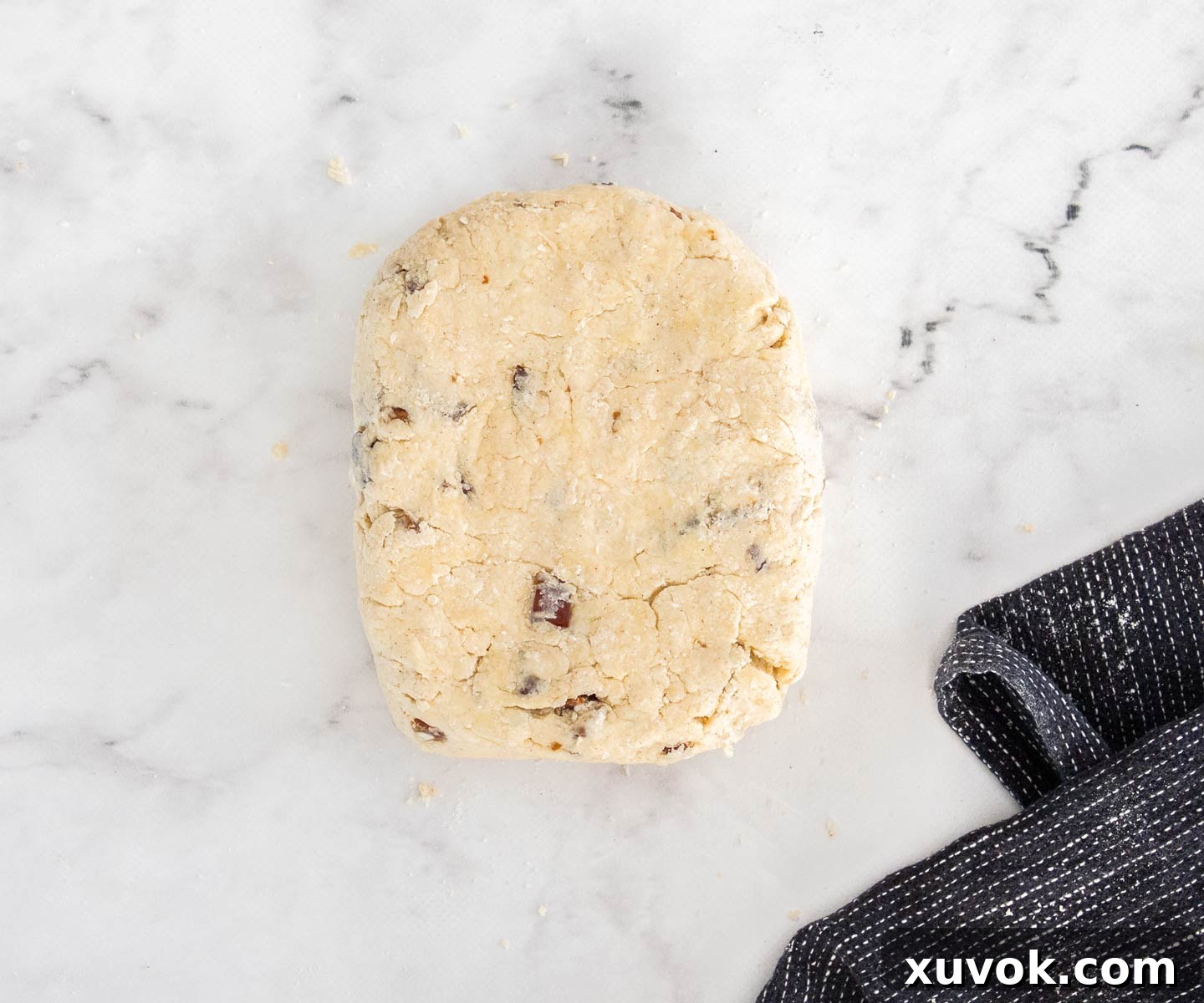 The date scone dough shaped into a rectangle on a marble surface, ready for cutting.