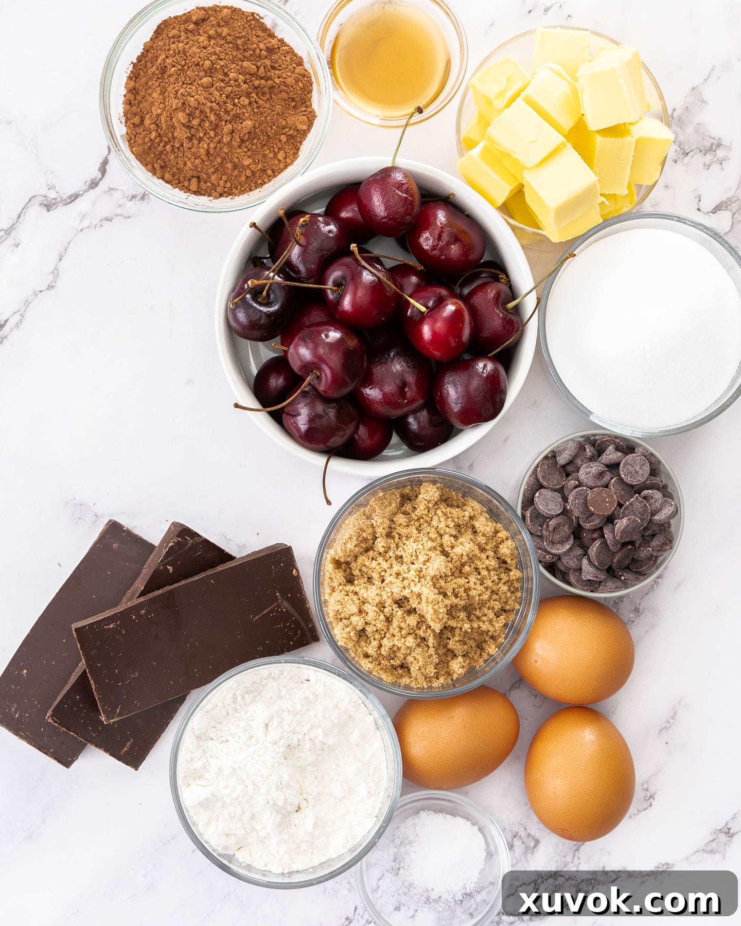 Ingredients for cherry brownies on a marble background, including fresh cherries, chocolate, and baking essentials.