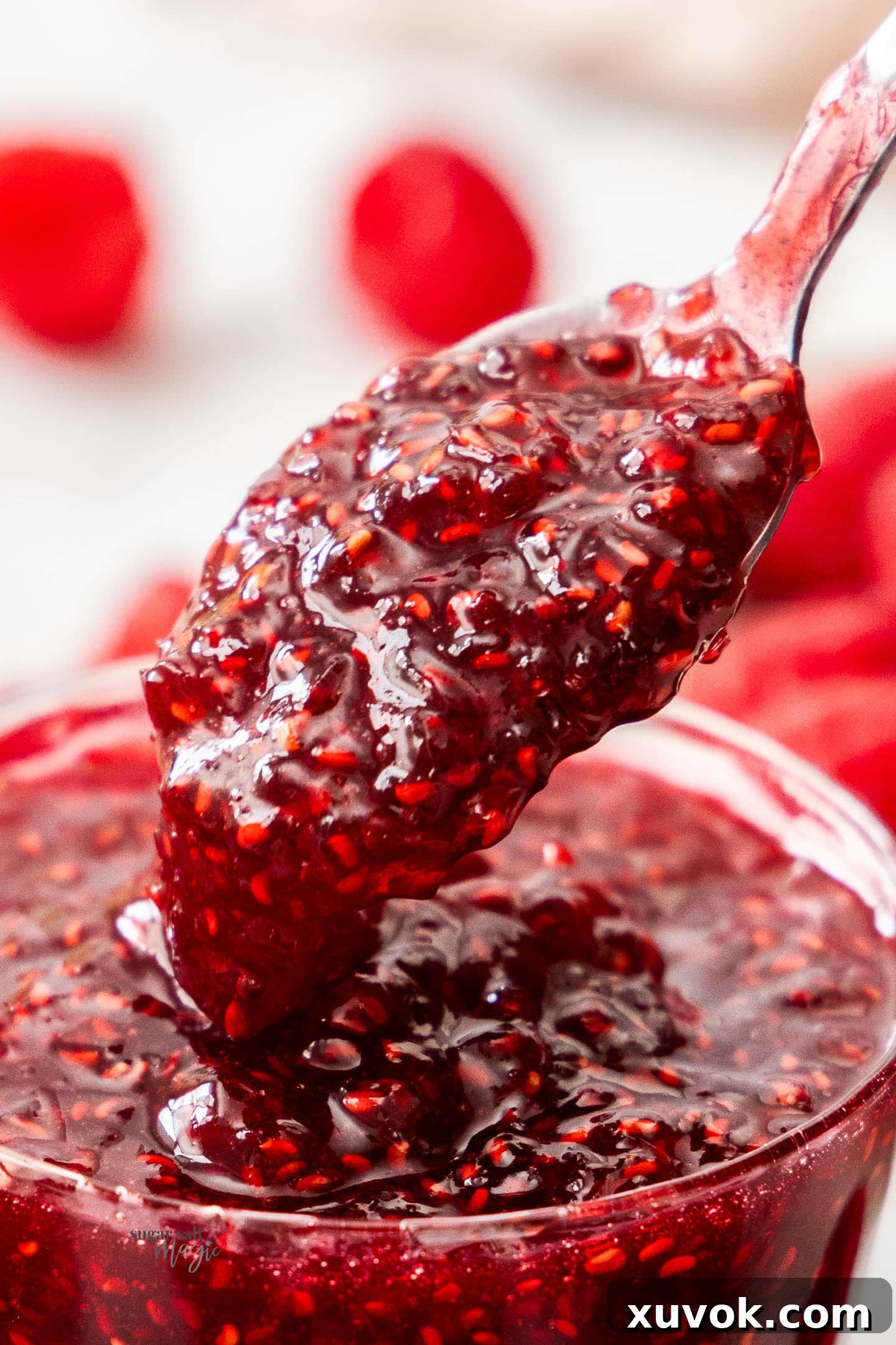 Extreme closeup of a spoonful of vibrant, ruby-red raspberry jam, showcasing its texture and rich color.