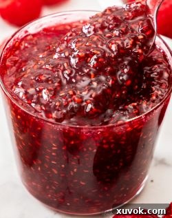 Looking into a glass of raspberry jam with a spoon digging in, showcasing its appealing texture and rich color.