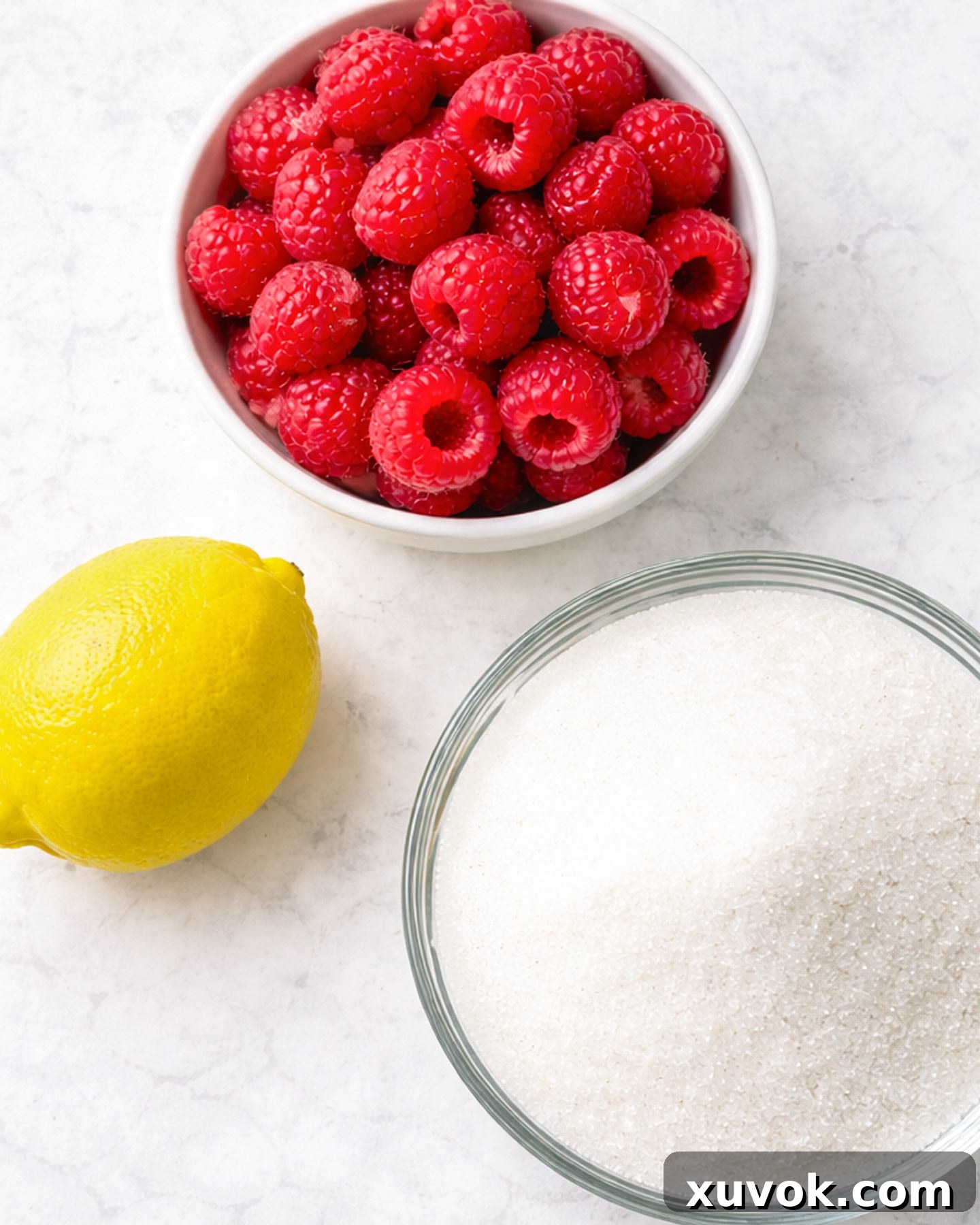 Ingredients for homemade raspberry jam artfully arranged on a clean marble surface.