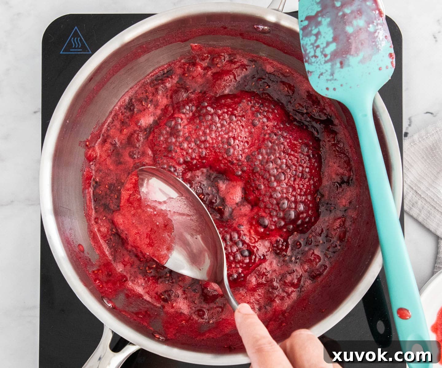 Scooping the residue off the bubbling raspberry jam in a saucepan to ensure a clear, vibrant finish.