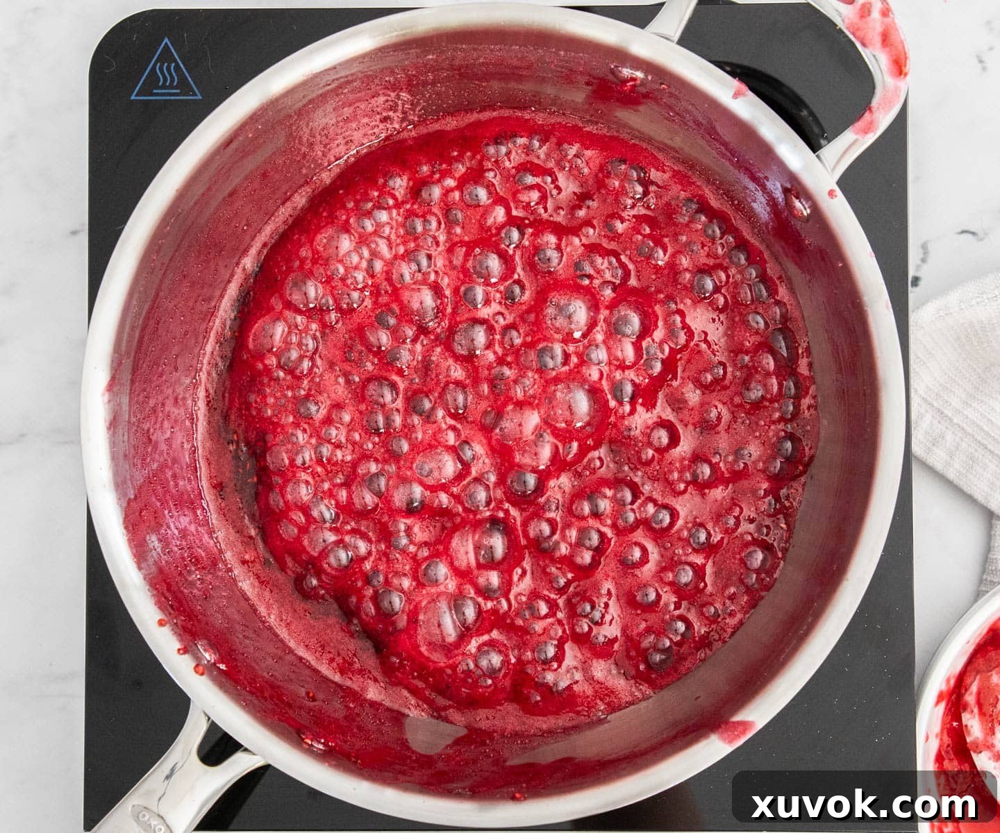The raspberry jam bubbling vigorously in a saucepan, beginning to reduce and thicken.