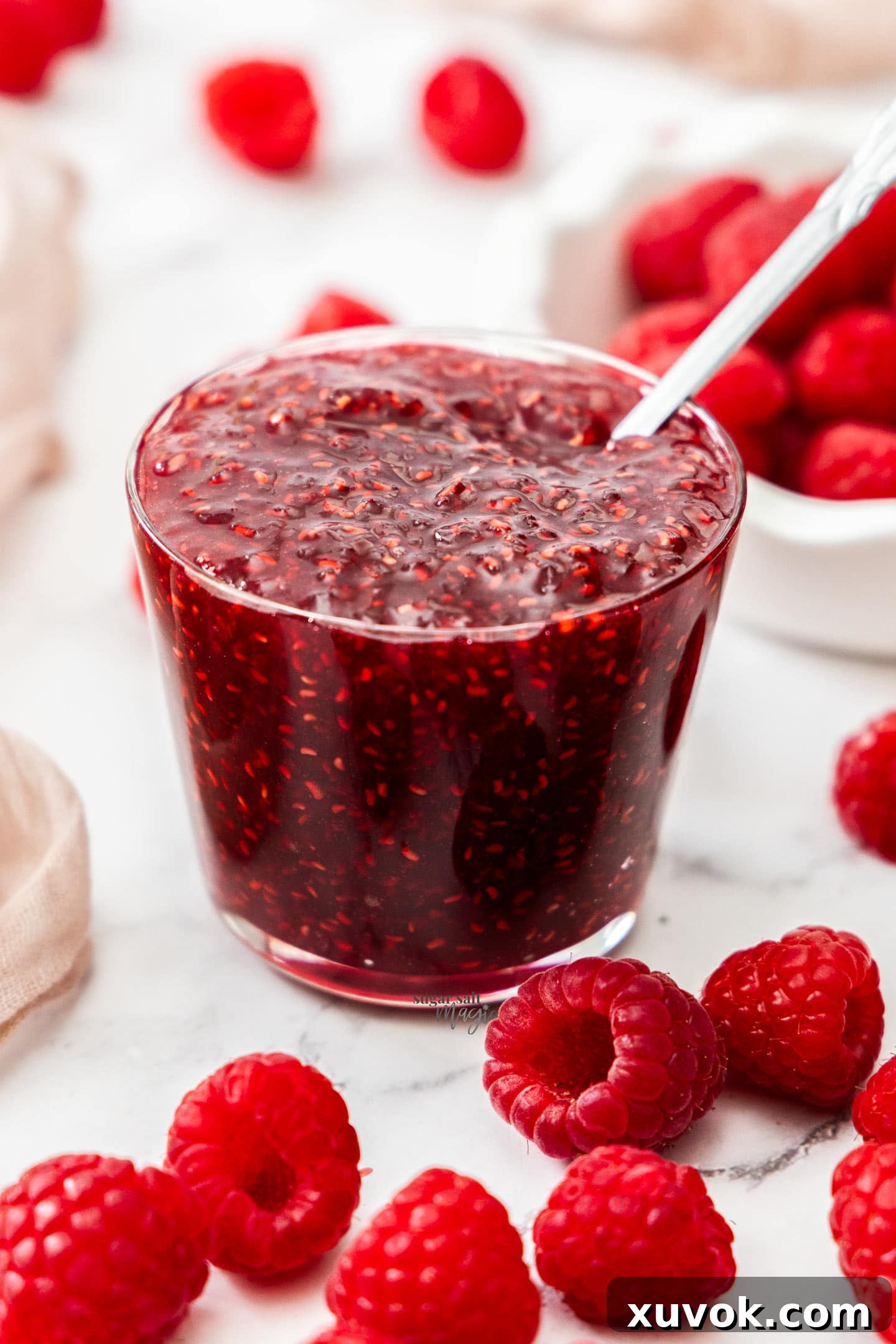 A tall glass jar filled to the brim with vibrant, homemade raspberry jam.
