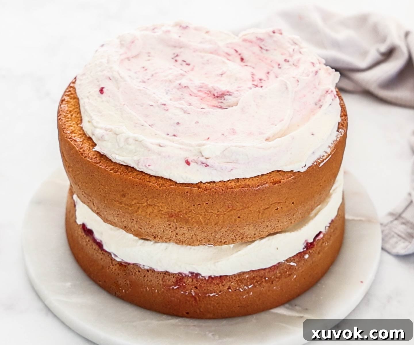 The two layers of raspberry sponge cake filled and topped with Chantilly cream and homemade raspberry jam, ready for serving.