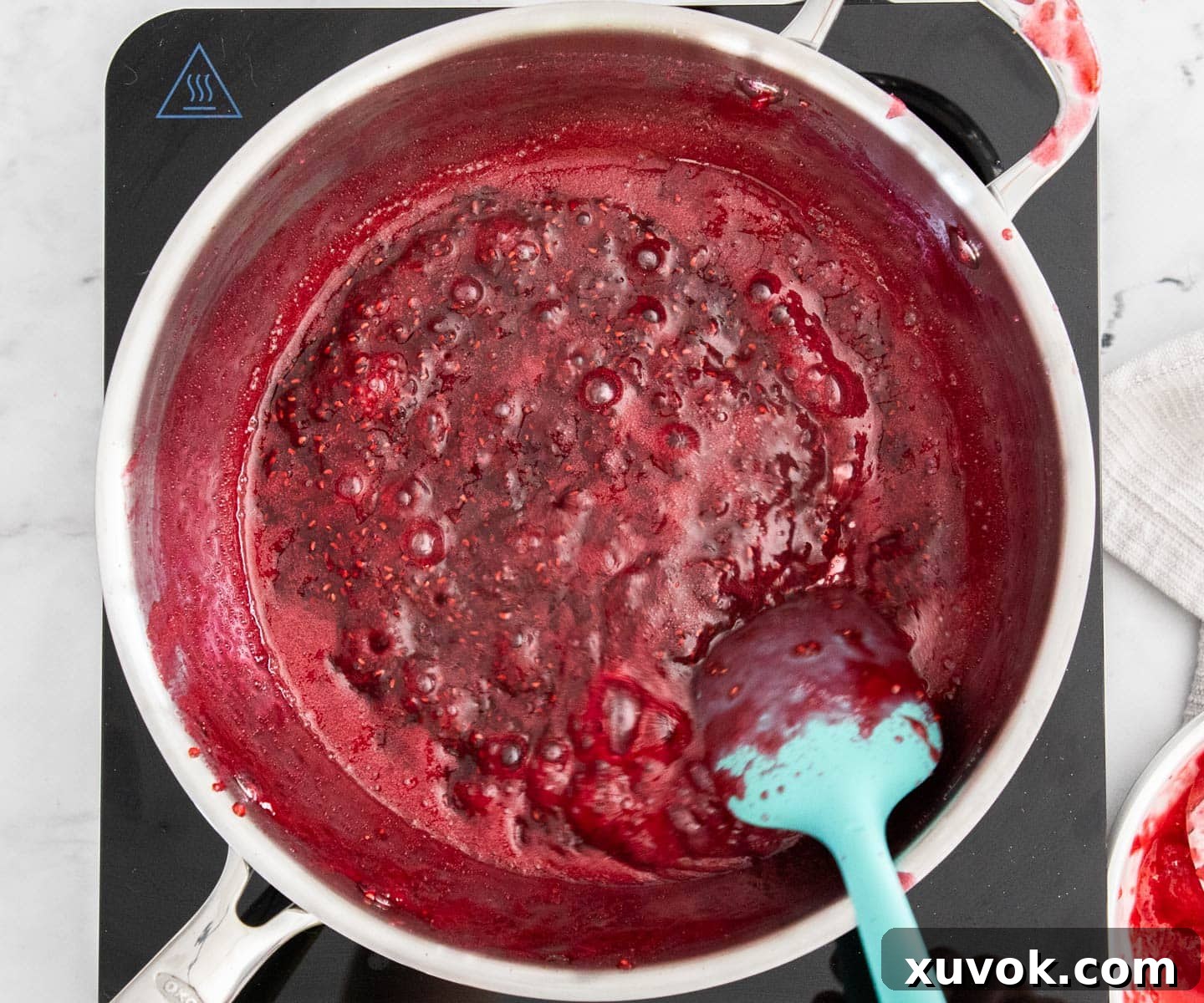 Close-up of thick raspberry jam simmering in a saucepan, showing its rich texture.