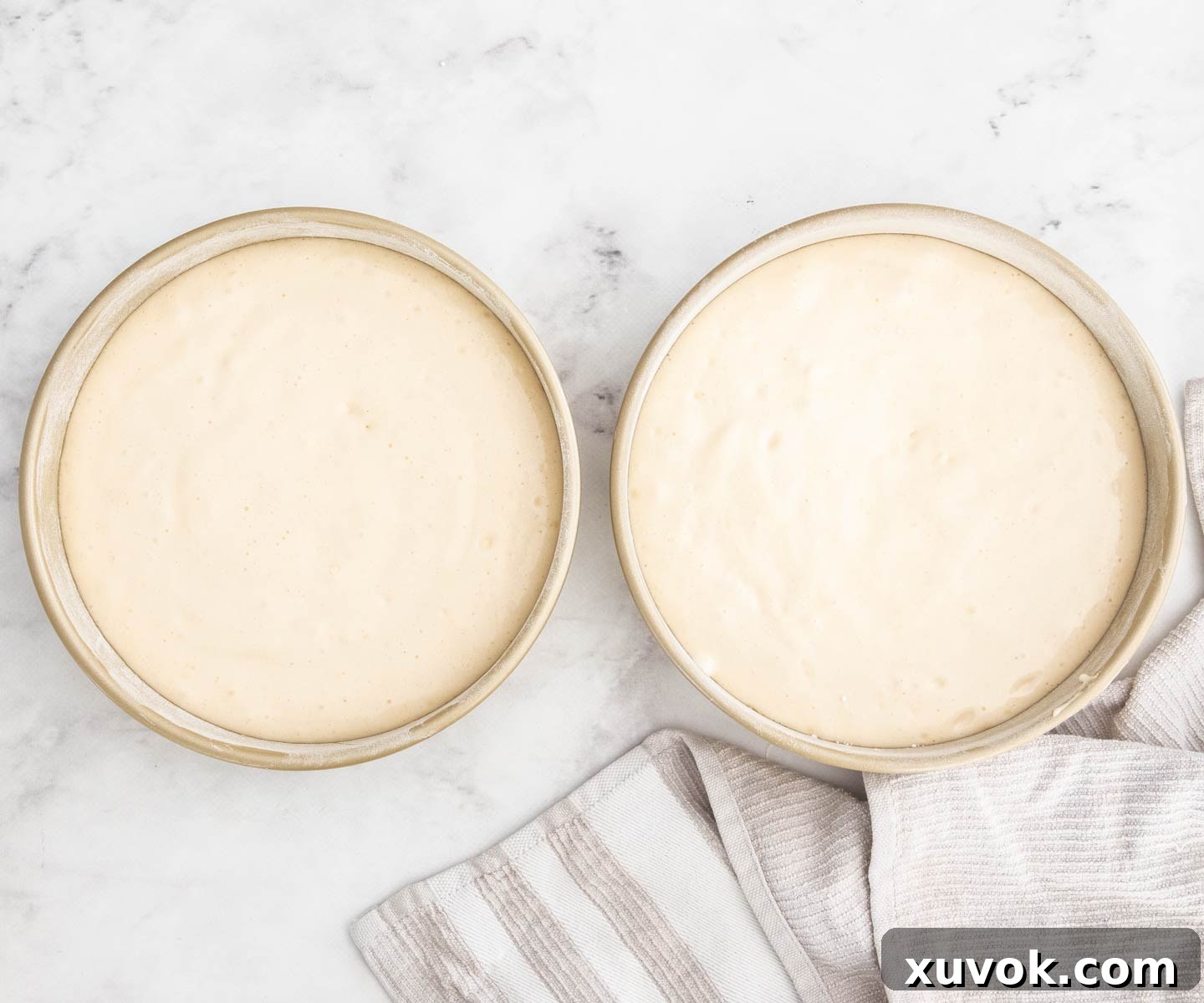 Two round baking pans filled with light, airy sponge cake batter, ready for the oven.
