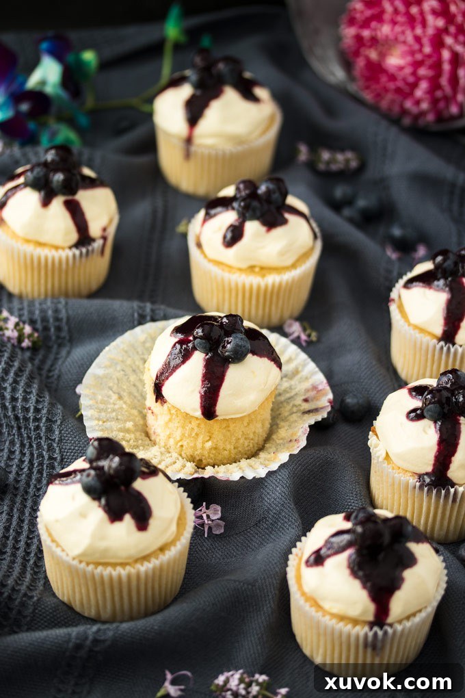 A Lemon Blueberry Cupcake with its paper peeled off, surrounded by more delectable cupcakes.
