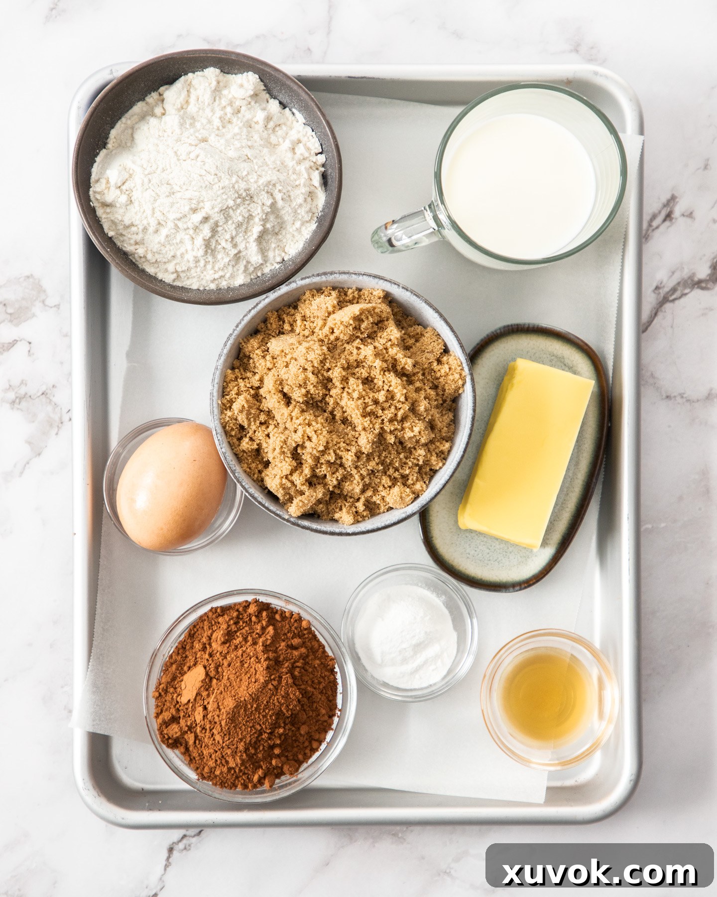 A beautifully arranged collection of fresh ingredients for chocolate self-saucing pudding laid out on a baking tray, ready for preparation.