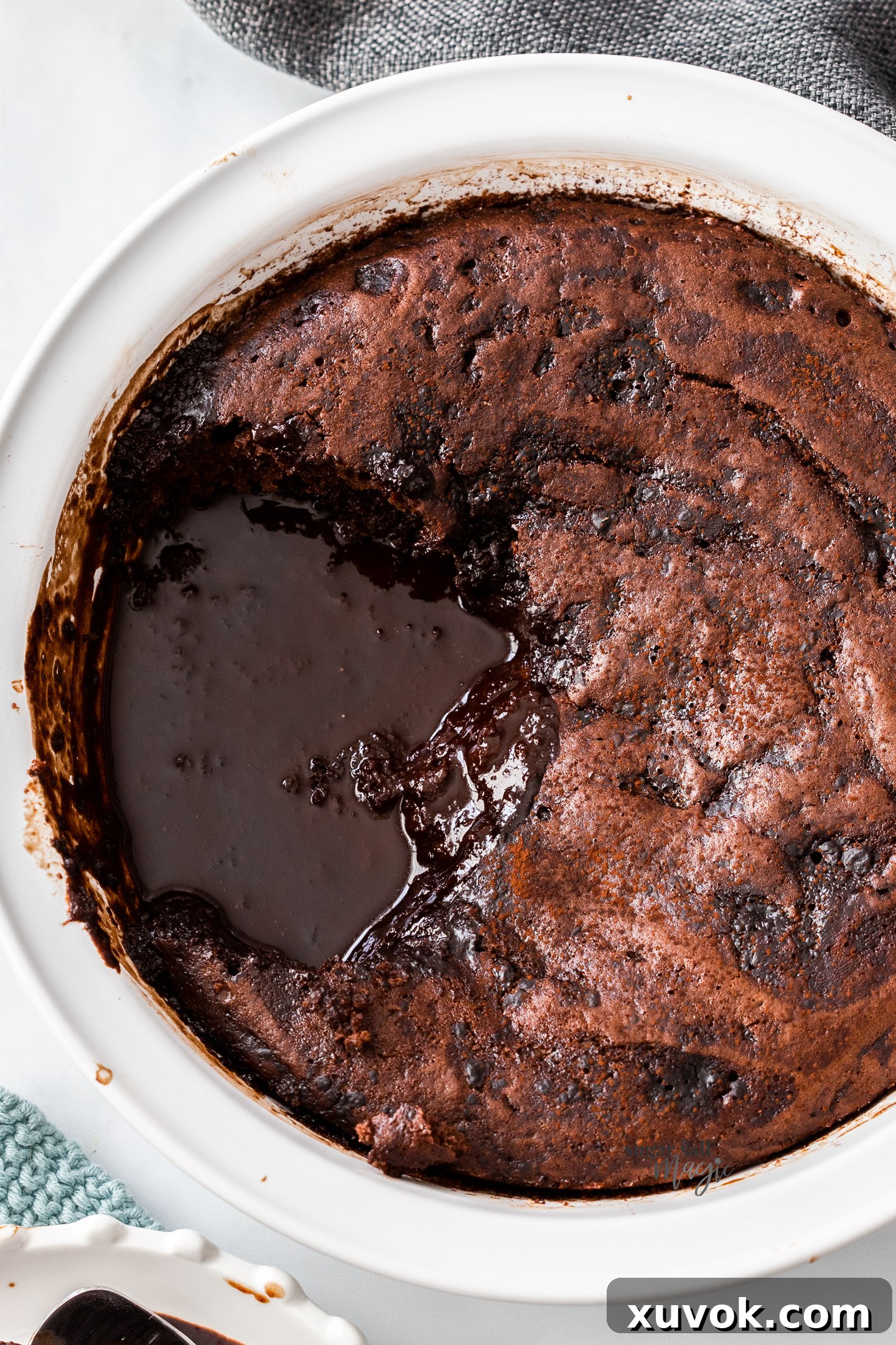 Close-up, top-down view of the baked self-saucing chocolate pudding, showing a glossy, rich pool of molten chocolate sauce emerging tantalizingly at the bottom.