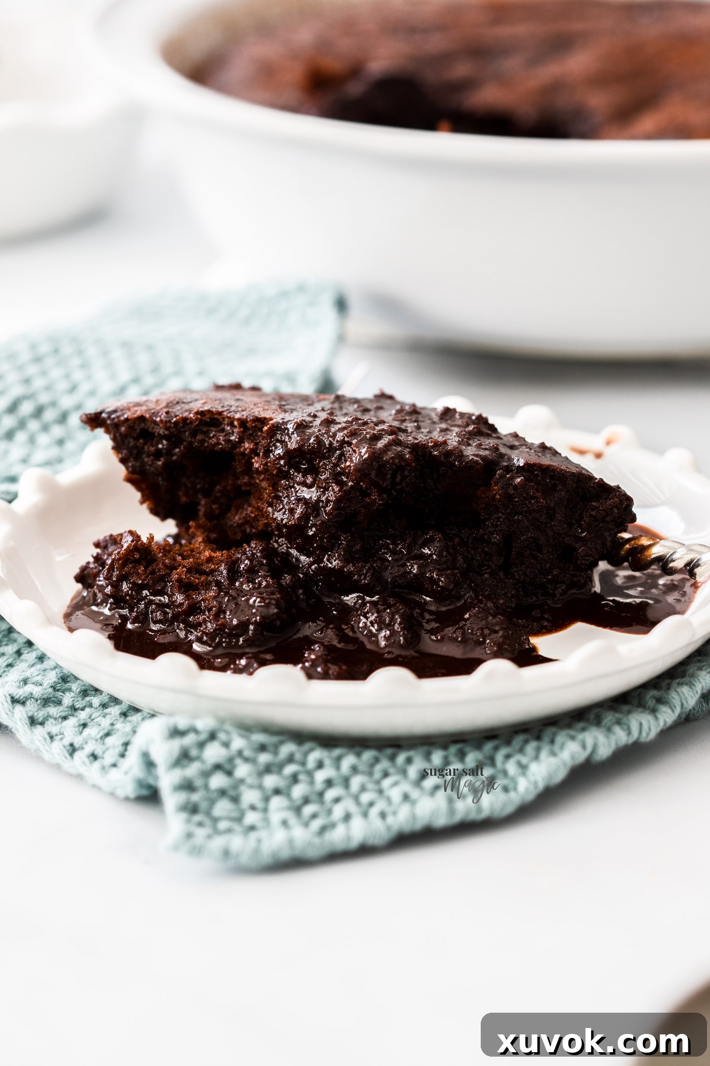 A perfectly scooped portion of rich chocolate self-saucing pudding presented on a dessert plate, with a generous pool of glossy, molten sauce visible around the tender cake.