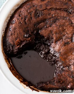 A serving of chocolate self-saucing pudding, freshly scooped from the dish, with a generous pool of molten chocolate sauce visible beneath.