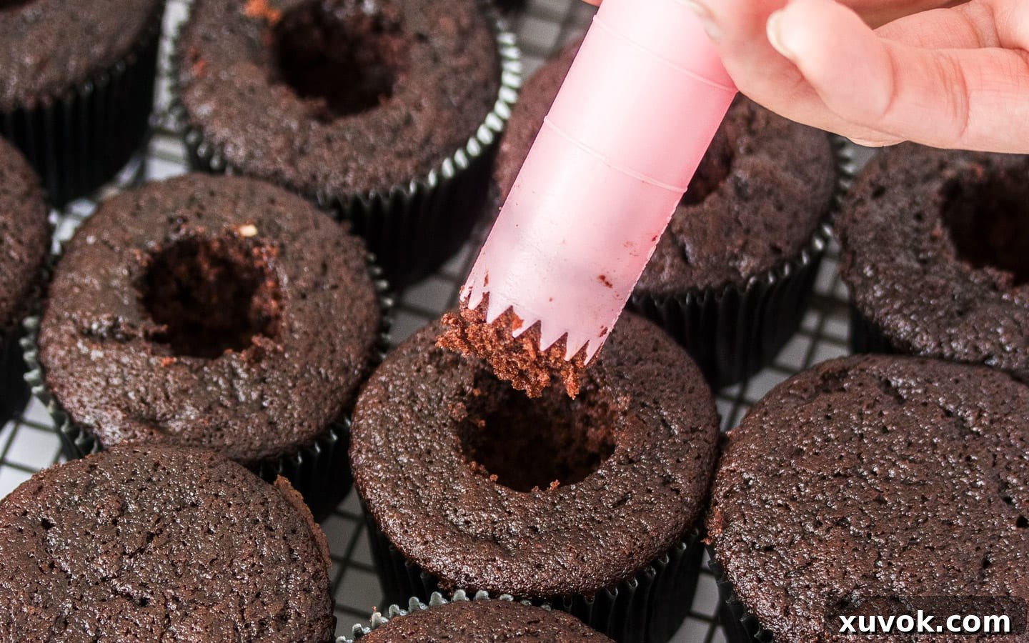 A pink cupcake corer expertly removing the center core from a chocolate cupcake, preparing it for a delicious ganache filling.