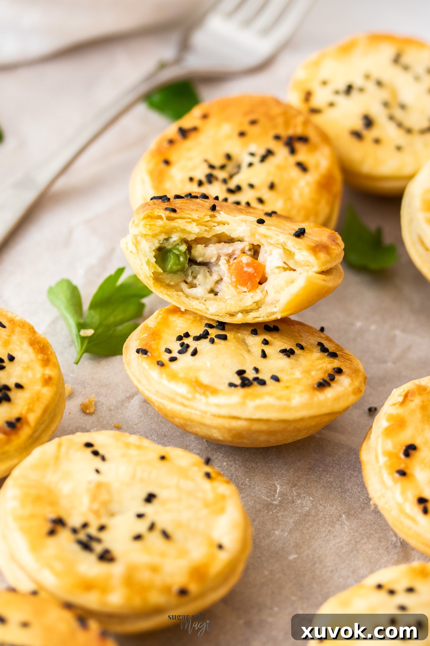 A perfectly golden-brown mini chicken pot pie, broken in half to reveal its creamy, delicious filling of chicken and mixed vegetables. It rests on top of a whole, intact mini pot pie, showcasing its inviting appearance.