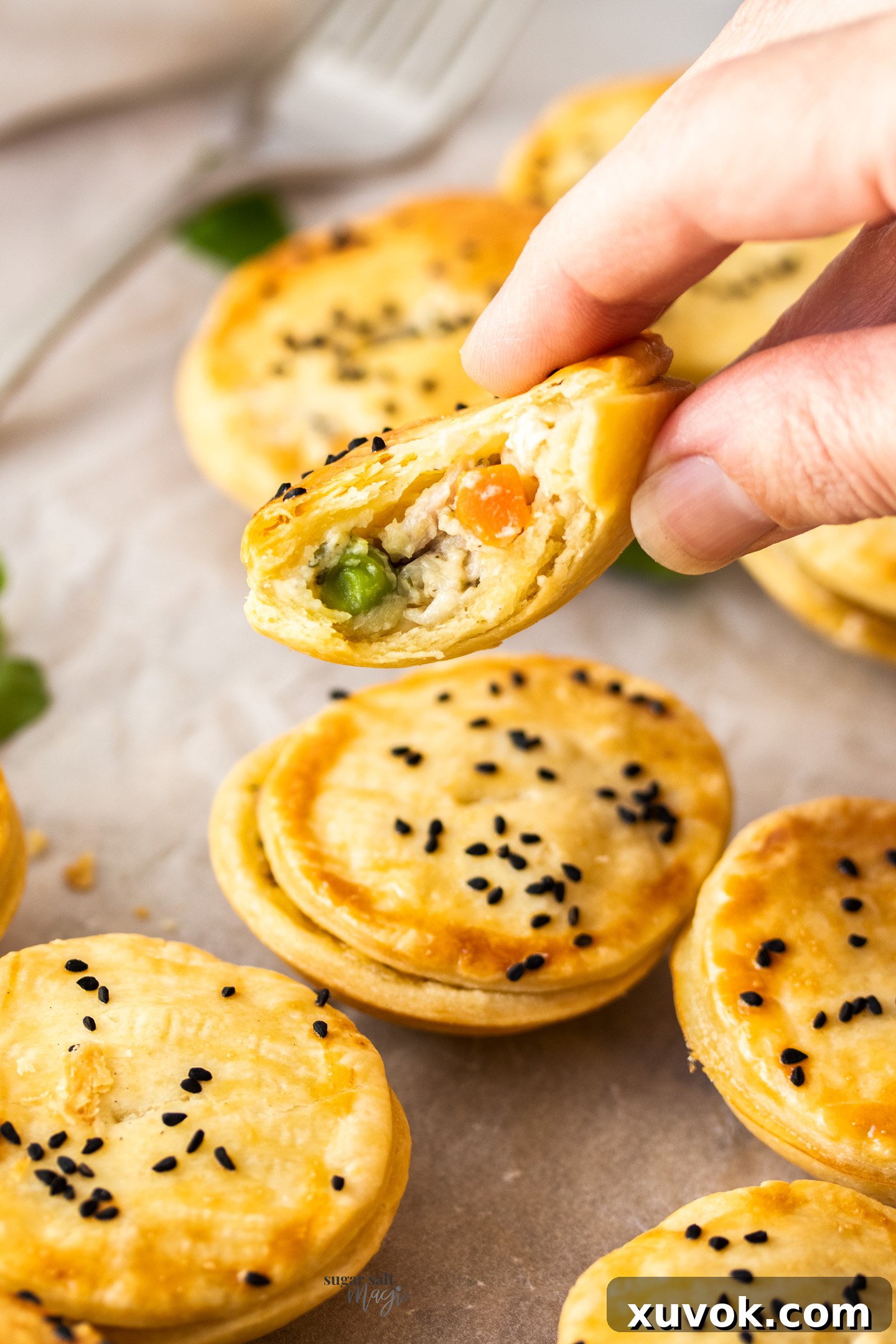 A hand holds a perfectly baked mini chicken pot pie, broken open to reveal the rich, creamy chicken and vegetable filling, steam gently rising.