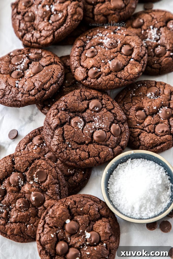 A batch of chocolate cookies piled next to a small dish of salt flakes.